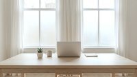 Minimalist workspace with laptop on wooden desk near bright windows. Clean home office setup with plant and coffee cup for productivity and remote work.