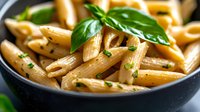 Penne pasta garnished with fresh basil leaves and herbs in dark bowl, close up view. Cooked al dente Italian cuisine with olive oil and parsley.
