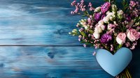 Fresh spring bouquet with pink roses and mixed flowers in heart-shaped vase against rustic blue wooden background, romantic floral arrangement for valentines day or wedding.