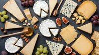 Gourmet cheese platter with variety of artisanal cheeses, fresh grapes, figs, nuts and honey on dark slate background for entertaining and culinary use.