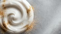 Creamy white swirl with golden cinnamon powder dusting on marble surface for culinary and food design projects.
