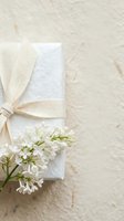 Elegant gift box wrapped in white textured paper with a beige linen bow and white lilac flowers on a neutral background.