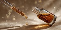 Golden honey dripping from glass dropper into small bottle on textured surface with warm bokeh lights creating luxurious spa and wellness atmosphere.