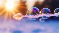 Iridescent soap bubbles with glittering frost crystals floating in winter sunlight against blurred blue background, creating magical macro photography effect.