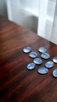 Iridescent glass cabochons scattered on dark wooden surface near window with natural light creating rainbow reflections for jewelry making crafts.