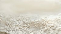 Delicate white lace trim with intricate floral patterns on soft fabric background for wedding dress details, bridal accessories, and romantic textile designs.