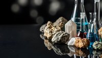Laboratory glassware with natural mineral specimens and crystals on reflective surface for scientific research and geological study applications.