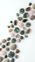Polished gemstones and healing crystals arranged in diagonal pattern on white background, including rose quartz, moss agate, and jasper for wellness and meditation design projects.