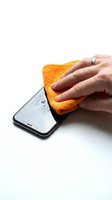 Hand wiping water droplets from smartphone screen with yellow microfiber cloth. Cleaning and maintenance concept for device care and protection.