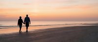 Romantic couple walking hand in hand on beach at sunset with golden sky and ocean waves, perfect for travel and relationship concepts.