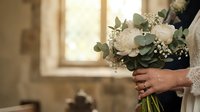 Bride holding elegant white rose bouquet with eucalyptus and baby's breath in soft natural light for wedding ceremony.