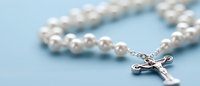 Catholic rosary with white pearl beads and silver crucifix on soft blue background, shallow depth of field creates gentle spiritual atmosphere.