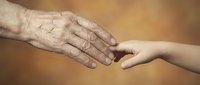 Elderly wrinkled hand gently touching young smooth hand in warm golden light representing intergenerational connection, care, support and family bonds.