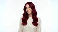Young woman with long burgundy red wavy hair smiling warmly in cream sweater against white background isolated for design use.