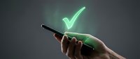 A hand holding a smartphone displaying a glowing neon green checkmark symbol, representing approval, success, and digital validation for app design and technology concepts.