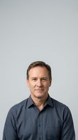 Middle-aged man with brown hair and Caucasian ethnicity wearing a dark blue button-up shirt against a neutral gray background. Suitable for corporate profiles, business websites, and professional headshots.