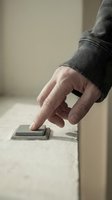 Mature male hand pressing light switch on beige wall, wearing gray sweater. Concept for electricity, home automation, energy control, and smart home technology applications.