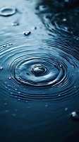 Concentric ripples forming on dark blue water surface with droplets creating circular patterns, suitable for environmental or wellness concepts.