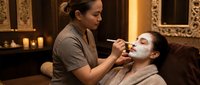 Professional spa therapist applying facial mask treatment to relaxed female client in luxury wellness center with warm ambient lighting and elegant decor.