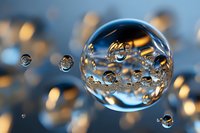 Macro photography of water drops with golden light reflections creating spherical formations against blurred blue background, showing surface tension and refraction.