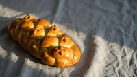Golden braided challah bread loaf with sesame seeds on linen cloth, traditional Jewish bakery product for holidays and Shabbat celebrations.