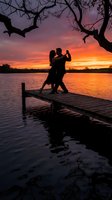 Romantic couple dancing on wooden dock at sunset over lake with dramatic purple orange sky and tree silhouette creating intimate moment for anniversary celebration.