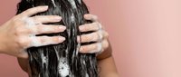 Woman applying hair mask treatment with hands massaging wet dark hair against pink background for healthy haircare routine.