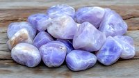 Polished purple amethyst tumbled stones arranged on rustic wooden surface, displaying natural crystal patterns and translucent lavender hues for spiritual healing.