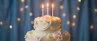 Elegant two-tier wedding cake with pink roses and lit candles against blue backdrop with golden bokeh lights for celebration and special occasions.