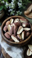 Raw and sliced Brazil nuts in wooden bowl with soft natural lighting, styled with white flowers for healthy eating and nutrition concept.
