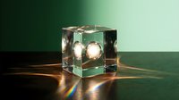 Glass cube with illuminated spheres casting warm light and colorful reflections on dark surface, suitable for modern design, backgrounds, and creative projects.