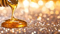 Golden honey or syrup pouring in slow motion against glittering bokeh background, creating luxurious flowing stream with amber reflections and sparkles.