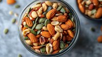 Mixed nuts and seeds in glass bowl including almonds cashews pumpkin seeds healthy snacking protein rich food ingredients for cooking and baking recipes.