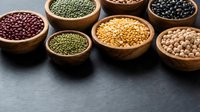 Assorted legumes and pulses in wooden bowls on dark slate surface showcasing variety of beans, lentils and chickpeas for healthy cooking and nutrition.