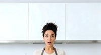 Woman with short dark hair and olive complexion wearing apron in modern kitchen. Chef or home cook preparing meals, ideal for culinary, cooking, and lifestyle content.