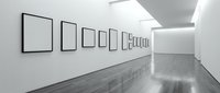 Empty white frames hanging on a bright gallery wall with polished hardwood floor, modern art exhibition interior with copy space.