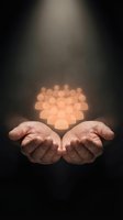 Cupped hands holding glowing heart-shaped bokeh lights against dark background symbolizing love, care, protection and compassion in spiritual healing concept.