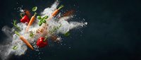Fresh vegetables and herbs exploding in a flour cloud on a dark background, capturing dynamic motion for food and culinary concepts.