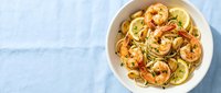 Shrimp pasta with lemon and garlic sauce served in white bowl on light blue surface, overhead view for restaurant menu or cooking blog.