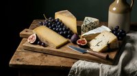 Assorted cheese selection with fresh figs and grapes on wooden board, wine bottle and linen cloth, gourmet food styling for culinary and entertaining content.