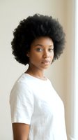 Young African American woman with natural afro hairstyle wearing white t-shirt looking at camera with confident expression in neutral indoor setting.
