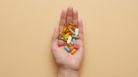 Caucasian hand holding assorted pharmaceutical pills, capsules, and tablets on neutral beige background. Healthcare and medicine concept for pharmaceutical industry, wellness, and medical treatment.