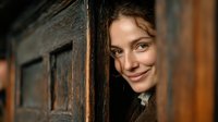 Young woman peeking through wooden door with warm smile and curious expression in cozy indoor setting with natural lighting and rustic architecture elements.