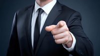 Businessman in dark suit pointing finger directly at viewer against navy background, conveying leadership and recruitment concept.