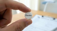 Hand holding placebo pill tablet in medical research clinical trial pharmaceutical testing environment with blurred laboratory background.