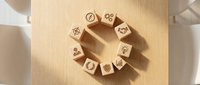 Wooden blocks arranged in circle with zodiac symbols on light wood surface, casting shadows in natural sunlight for astrology and horoscope concepts.