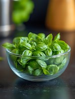 Fresh green basil leaves in glass bowl on dark background, selective focus with soft bokeh. Aromatic herb for cooking and garnishing dishes.