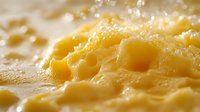 Macro shot of melted cheese texture showing holes and bubbles in yellow dairy product, close up food photography with soft focus and natural lighting.