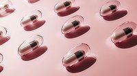 Transparent capsules with black content casting shadows on pink background, arranged in repeating pattern for cosmetic and pharmaceutical design projects.