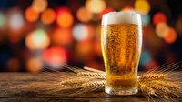 Fresh golden beer glass with foam on wooden table with wheat ears against warm bokeh lights background for pub and brewery concepts.